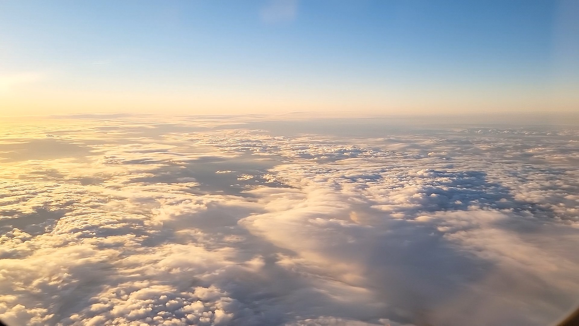 A luminous morning cloud deck seen from cruise altitude, pale gold light over soft clouds