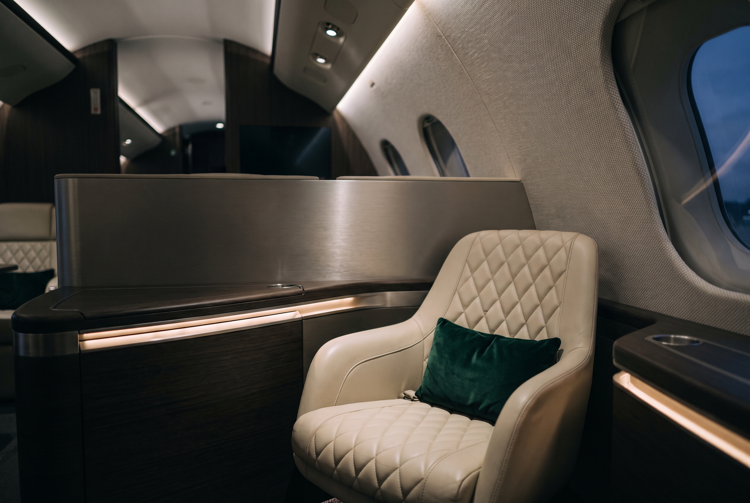 A modern first-class seat in cream leather with a green pillow